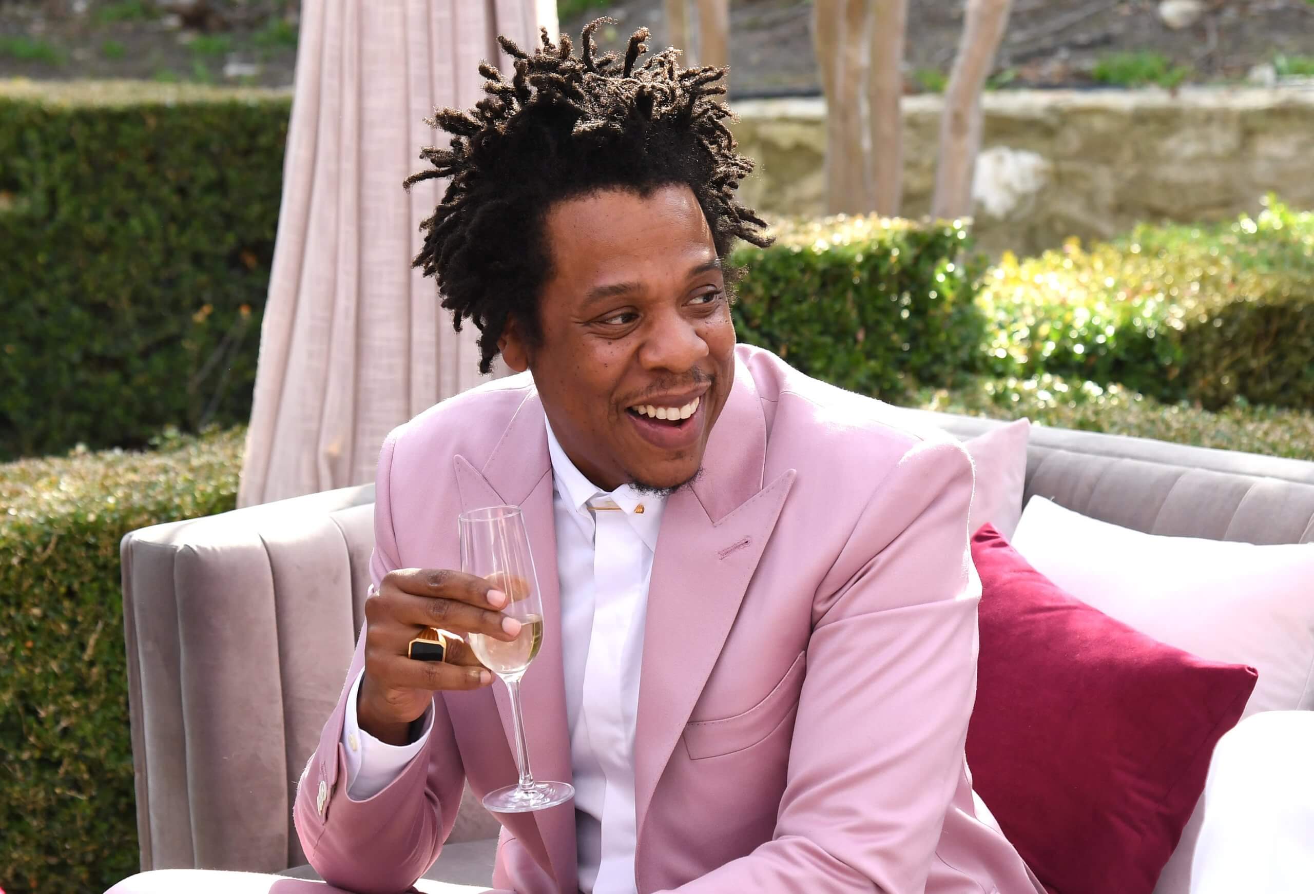 Foto van Jay-Z in een roze pak die een glas champagne vast houdt